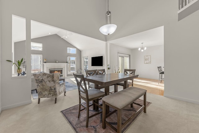 dining space featuring high vaulted ceiling, plenty of natural light, a lit fireplace, and baseboards