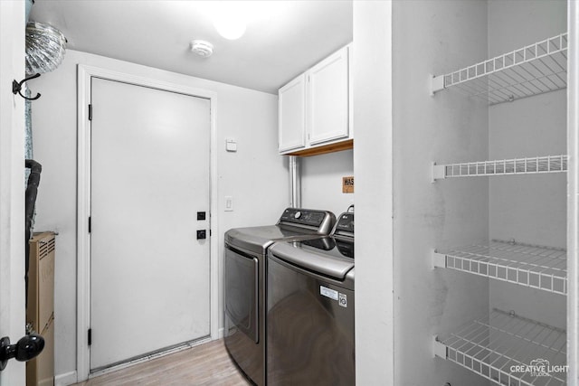 clothes washing area featuring separate washer and dryer, light hardwood / wood-style flooring, and cabinets