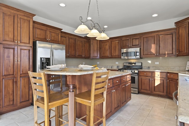 kitchen featuring a kitchen island, appliances with stainless steel finishes, decorative light fixtures, decorative backsplash, and light stone counters