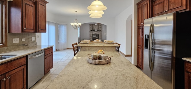 kitchen with appliances with stainless steel finishes, pendant lighting, tasteful backsplash, a large fireplace, and light stone countertops