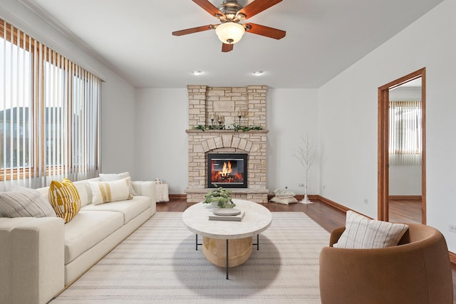 living room featuring ceiling fan, a stone fireplace, and light hardwood / wood-style floors