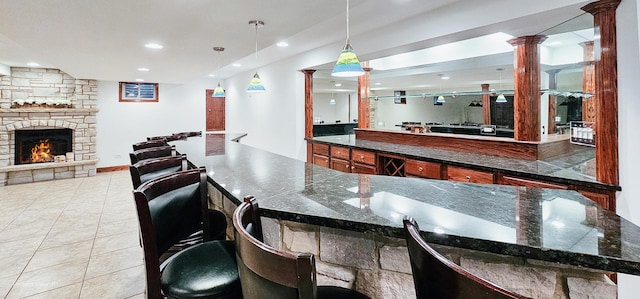 kitchen featuring a breakfast bar area, ornate columns, decorative light fixtures, light tile patterned floors, and a fireplace