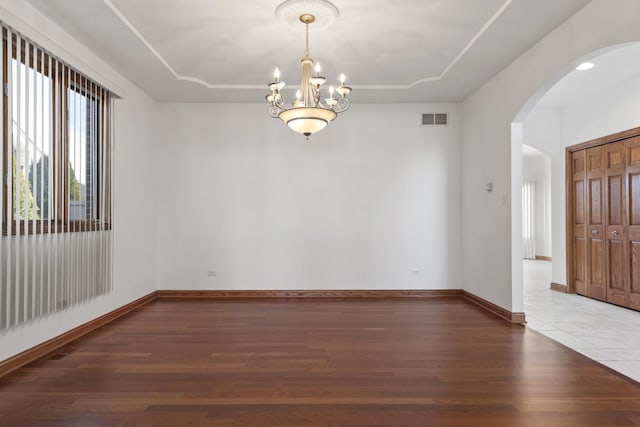 unfurnished room featuring a raised ceiling, wood-type flooring, and an inviting chandelier