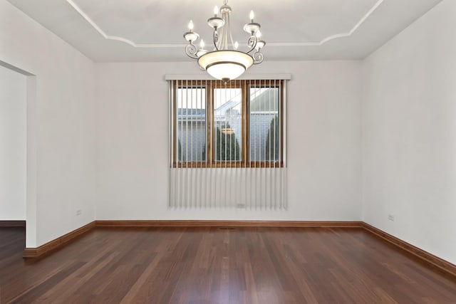 empty room featuring an inviting chandelier, dark hardwood / wood-style floors, and a raised ceiling