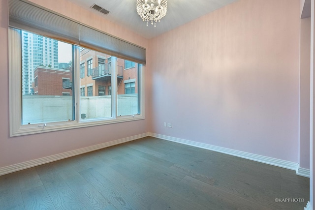 empty room featuring wood-type flooring and a notable chandelier