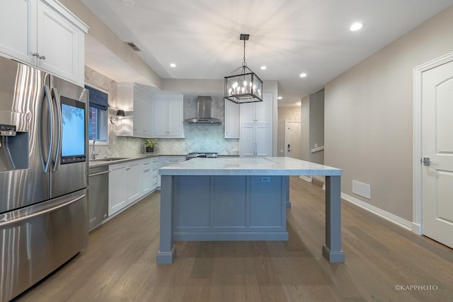 kitchen with white cabinetry, hanging light fixtures, a kitchen island, stainless steel appliances, and wall chimney range hood