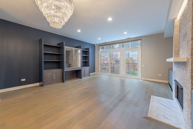 unfurnished living room with built in features, a notable chandelier, and light hardwood / wood-style floors