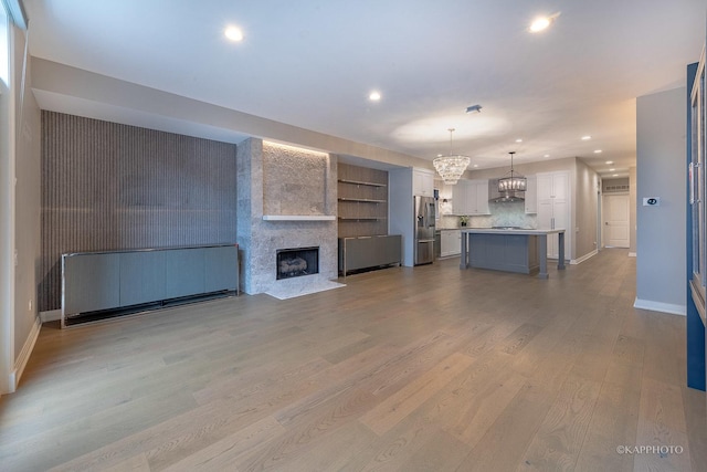 unfurnished living room featuring a fireplace, a chandelier, and light wood-type flooring