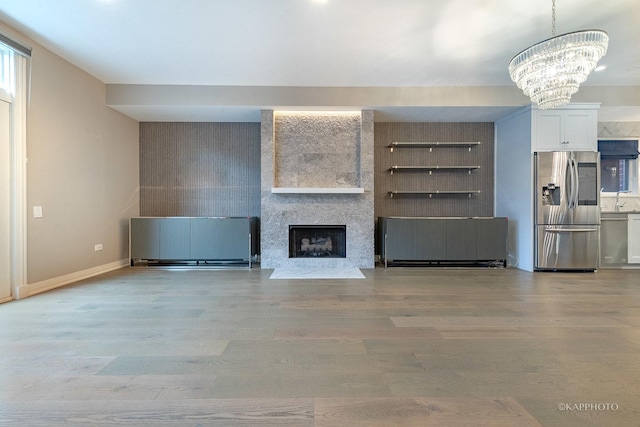 unfurnished living room featuring a notable chandelier, sink, light hardwood / wood-style flooring, and a large fireplace