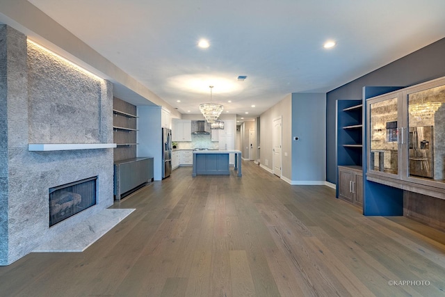 unfurnished living room with an inviting chandelier, built in shelves, a fireplace, and dark hardwood / wood-style floors