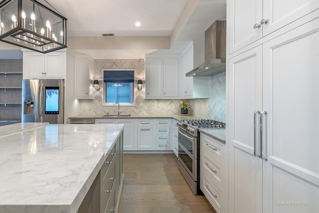 kitchen featuring sink, appliances with stainless steel finishes, white cabinetry, hanging light fixtures, and wall chimney exhaust hood