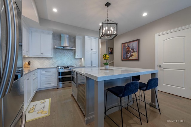 kitchen with stainless steel appliances, white cabinetry, a kitchen island, and wall chimney exhaust hood