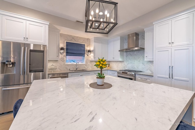 kitchen with appliances with stainless steel finishes, pendant lighting, sink, light stone countertops, and wall chimney range hood