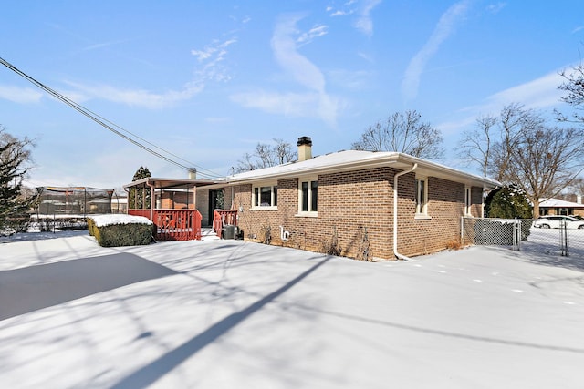 snow covered property with brick siding, a trampoline, and fence