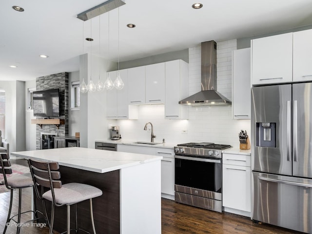 kitchen featuring pendant lighting, white cabinets, a center island, stainless steel appliances, and wall chimney exhaust hood