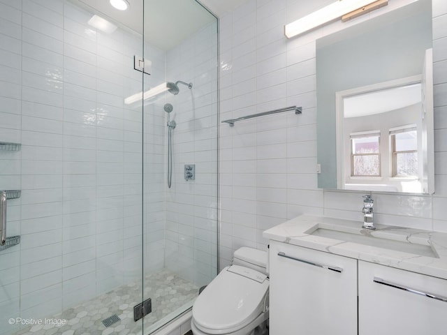 bathroom with a shower with door, vanity, tile walls, and toilet