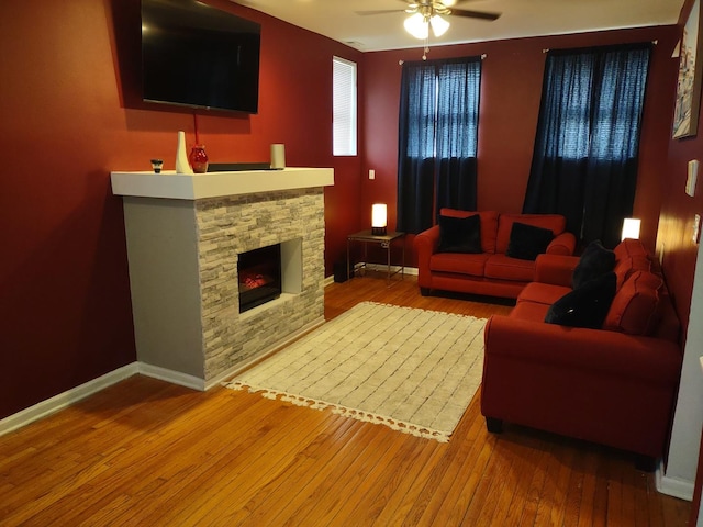 living room featuring hardwood / wood-style flooring, ceiling fan, and a stone fireplace