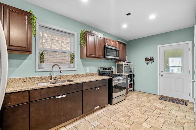 kitchen featuring stainless steel appliances, light stone countertops, sink, and dark brown cabinets