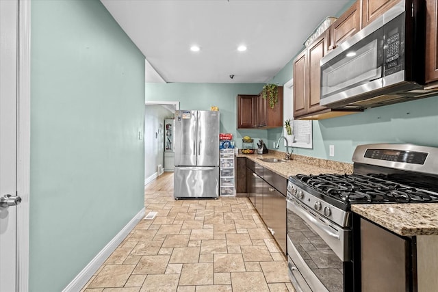 kitchen with stainless steel appliances, light stone countertops, and sink