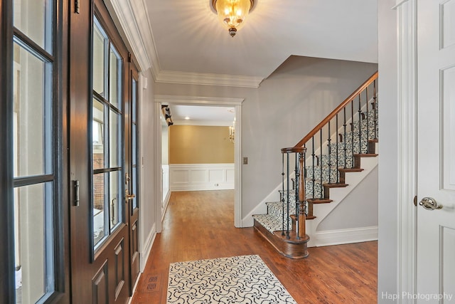 entryway featuring visible vents, a wainscoted wall, stairway, ornamental molding, and wood finished floors