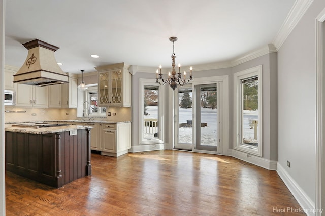 kitchen with glass insert cabinets, island range hood, appliances with stainless steel finishes, light stone countertops, and decorative light fixtures