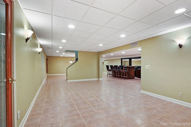 finished basement featuring baseboards, visible vents, a drop ceiling, and light tile patterned flooring