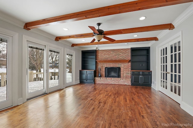 unfurnished living room with built in shelves, wood finished floors, a brick fireplace, beamed ceiling, and crown molding