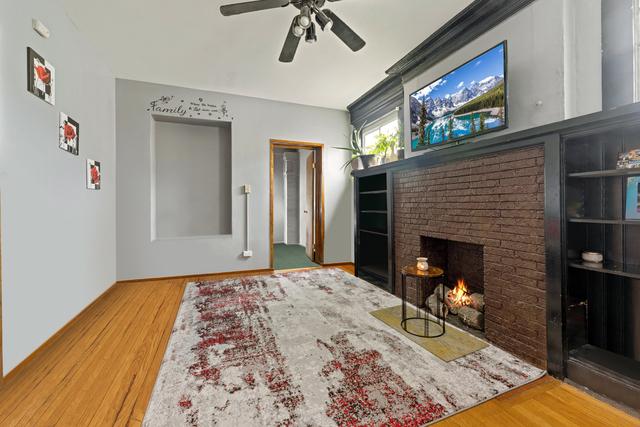 living room with a brick fireplace, hardwood / wood-style flooring, and ceiling fan