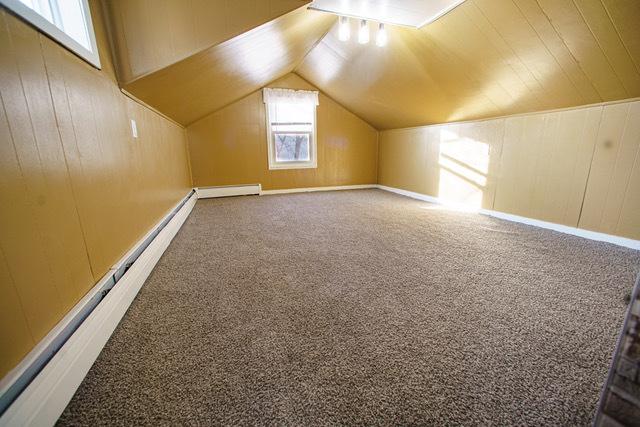 bonus room featuring a baseboard heating unit, carpet floors, wooden walls, and vaulted ceiling