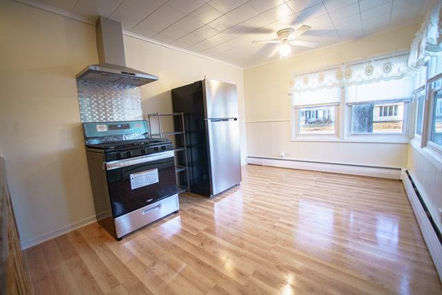 kitchen with light hardwood / wood-style floors, appliances with stainless steel finishes, baseboard heating, and wall chimney exhaust hood