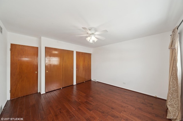 unfurnished bedroom featuring multiple closets, ceiling fan, and dark hardwood / wood-style flooring