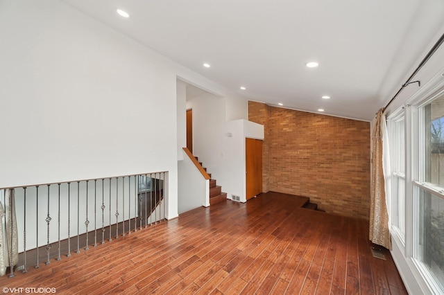 unfurnished room with hardwood / wood-style flooring, lofted ceiling, and brick wall