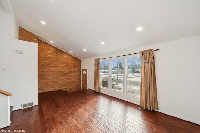 unfurnished living room with vaulted ceiling, dark hardwood / wood-style floors, and brick wall