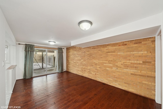 unfurnished room featuring dark wood-type flooring and brick wall