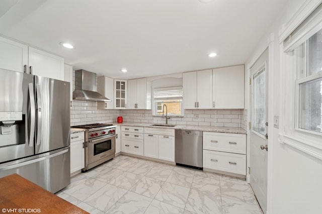 kitchen with white cabinetry, sink, light stone counters, stainless steel appliances, and wall chimney exhaust hood