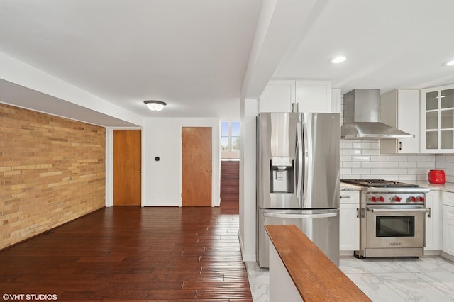 kitchen with brick wall, wall chimney exhaust hood, stainless steel appliances, and white cabinets