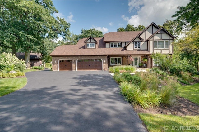 tudor home with a garage, aphalt driveway, and brick siding