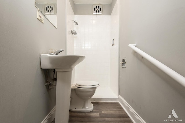 bathroom with hardwood / wood-style flooring, tiled shower, and toilet