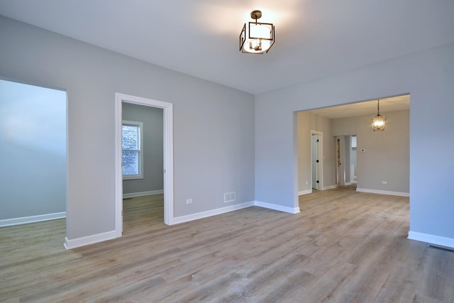 unfurnished room with a notable chandelier and light wood-type flooring