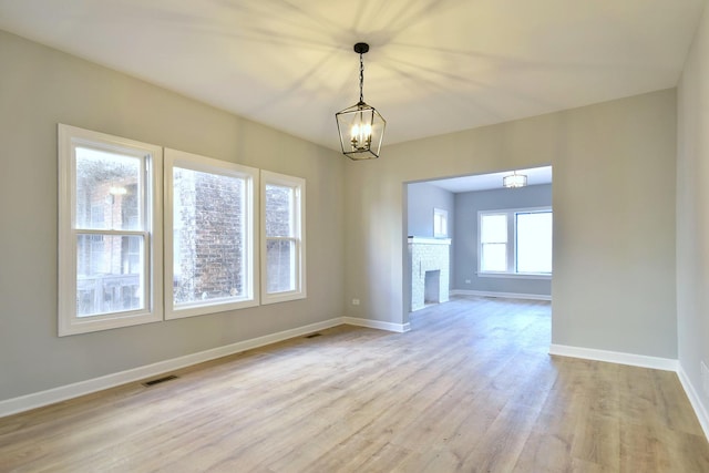 unfurnished dining area featuring light wood-type flooring, a fireplace, and a chandelier