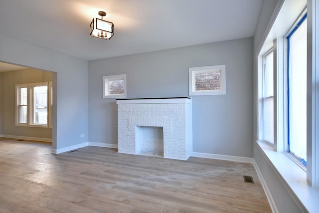 unfurnished living room featuring light hardwood / wood-style flooring, a brick fireplace, and a wealth of natural light