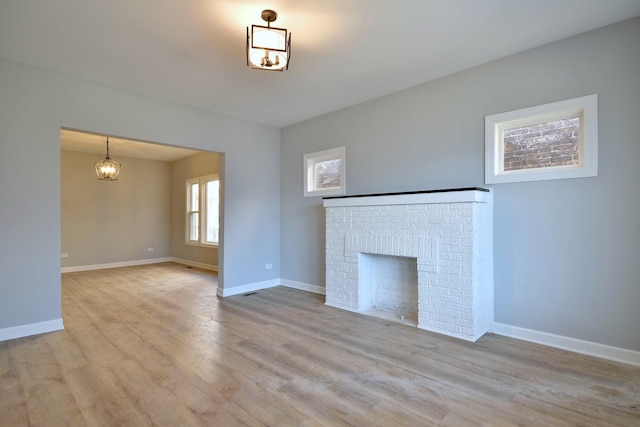 unfurnished living room featuring a brick fireplace, a chandelier, and light hardwood / wood-style flooring