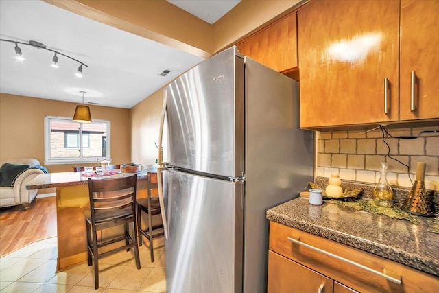 kitchen featuring stainless steel fridge, a breakfast bar, backsplash, light tile patterned flooring, and dark stone counters