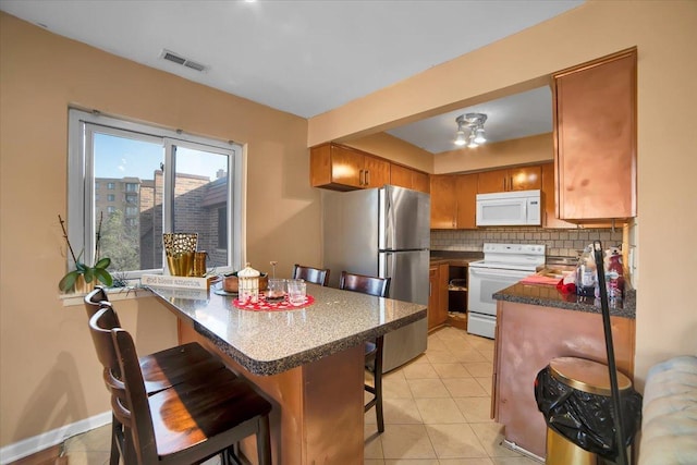 kitchen with a kitchen bar, tasteful backsplash, light tile patterned floors, kitchen peninsula, and white appliances