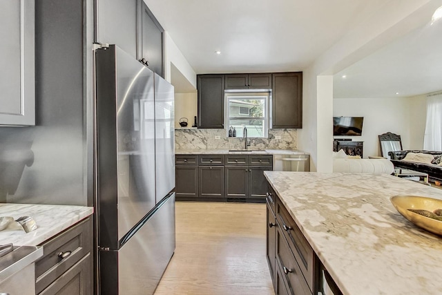 kitchen with sink, light hardwood / wood-style flooring, appliances with stainless steel finishes, backsplash, and dark brown cabinetry