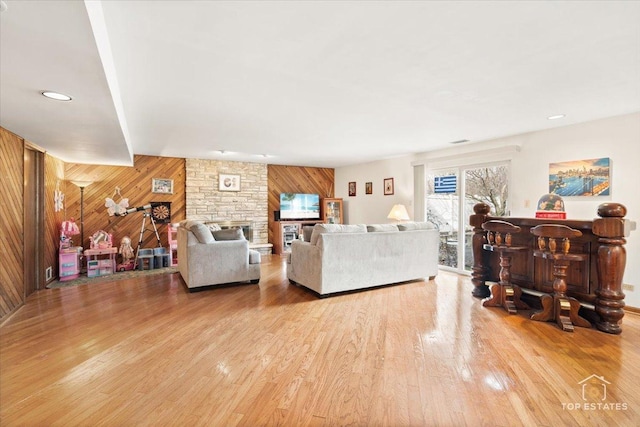 living room with a stone fireplace, light hardwood / wood-style floors, and wood walls