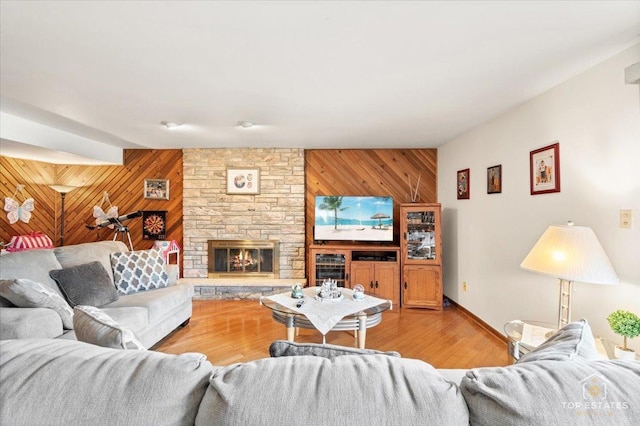 living room featuring a stone fireplace, light hardwood / wood-style flooring, and wood walls