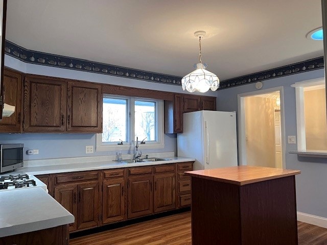 kitchen with sink, dark hardwood / wood-style floors, white fridge, a kitchen island, and pendant lighting