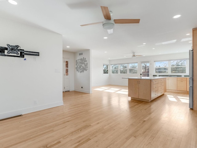 kitchen featuring light brown cabinetry, light hardwood / wood-style flooring, stainless steel refrigerator, a kitchen island, and ceiling fan