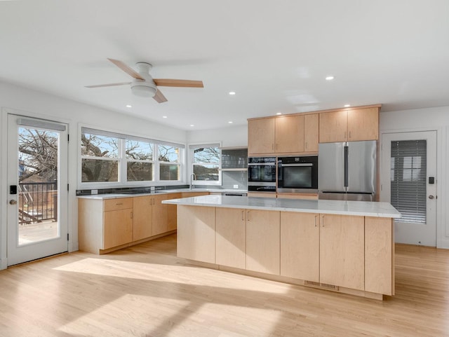 kitchen featuring light brown cabinetry, a center island, stainless steel fridge, double oven, and light hardwood / wood-style floors